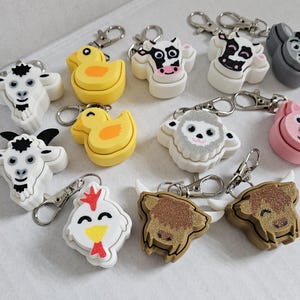 May include: A set of 10 colourful animal keyrings. Each keyring features a different animal, including a cow, pig, sheep, chicken, duck, and goat. The keyrings are made of plastic and have a metal ring for attaching to keys.