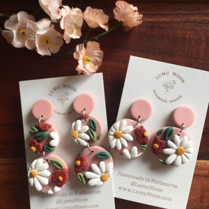 May include: A pair of pink and white floral dangle earrings with a pink background. The earrings are handmade in Melbourne, Australia. The earrings are made by Lumu Moon.