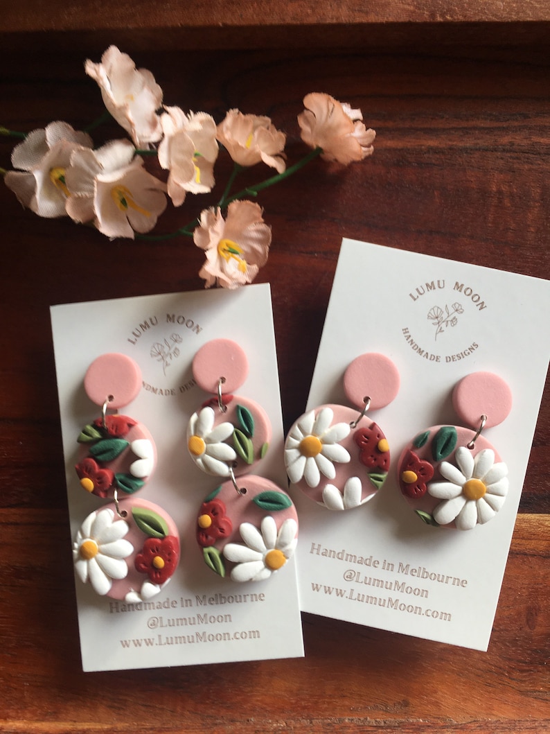 May include: A pair of pink and white floral dangle earrings with a pink background. The earrings are handmade in Melbourne, Australia. The earrings are made by Lumu Moon.