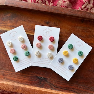 May include: Three sets of polymer clay earrings on white cards. Each set has three earrings with different colours and patterns. The colours are white, red, pink, green, yellow, and grey. The text on the cards reads "LUMU MOON Handmade Designs".