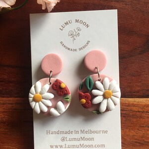 May include: A pair of pink and white floral polymer clay earrings with a white daisy and red flower design. The earrings are handmade in Melbourne, Australia by Lumu Moon Designs.