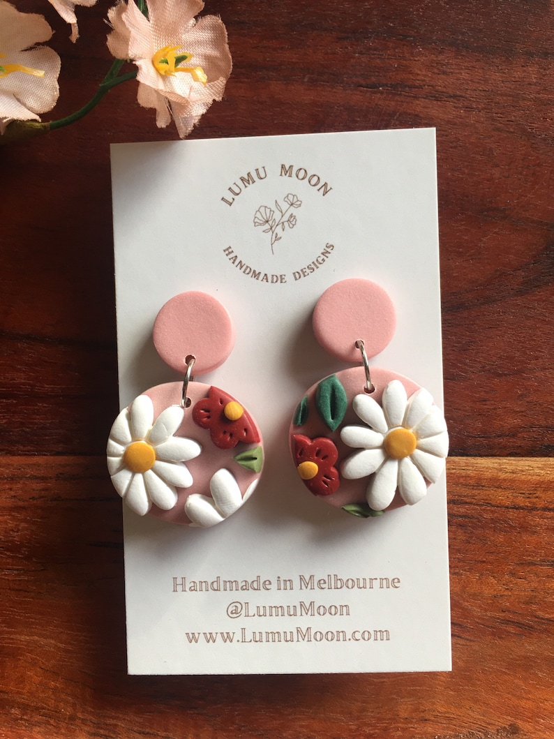 May include: A pair of pink and white floral polymer clay earrings with a white daisy and red flower design. The earrings are handmade in Melbourne, Australia by Lumu Moon Designs.