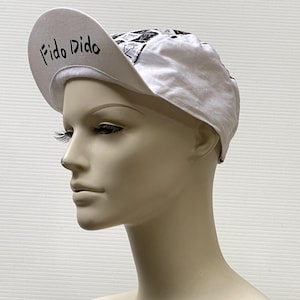 May include: White cycling cap with a black and white graphic print and the text "Fido Dido" on the front.