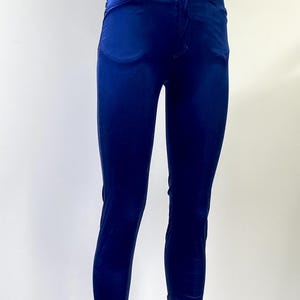 May include: A pair of high-waisted, form-fitting, navy blue velvet pants. The pants have a classic five-pocket design with a button and zipper closure. The fabric has a subtle sheen, and the pants are displayed on a mannequin.