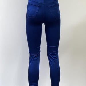 May include: A pair of form-fitting, royal blue jeans. The jeans have a high waist, back pockets, and a small leather patch with a logo on the back. The fabric appears to be a smooth, slightly shiny material.