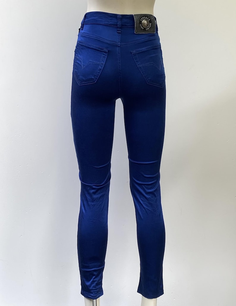 May include: A pair of form-fitting, royal blue jeans. The jeans have a high waist, back pockets, and a small leather patch with a logo on the back. The fabric appears to be a smooth, slightly shiny material.