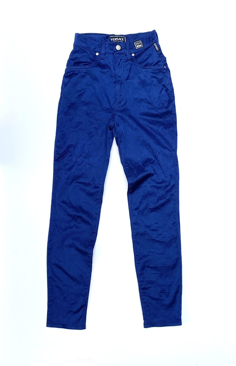 May include: A pair of blue denim pants with the Versace logo on the waistband. The pants have a classic five-pocket design and a button and zipper closure. The fabric appears to be a medium-weight denim.