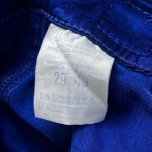 May include: Close-up of a white tag with the number 29 and 43 printed on it, sewn onto a vibrant blue fabric. The tag also includes text indicating the fabric composition and origin.