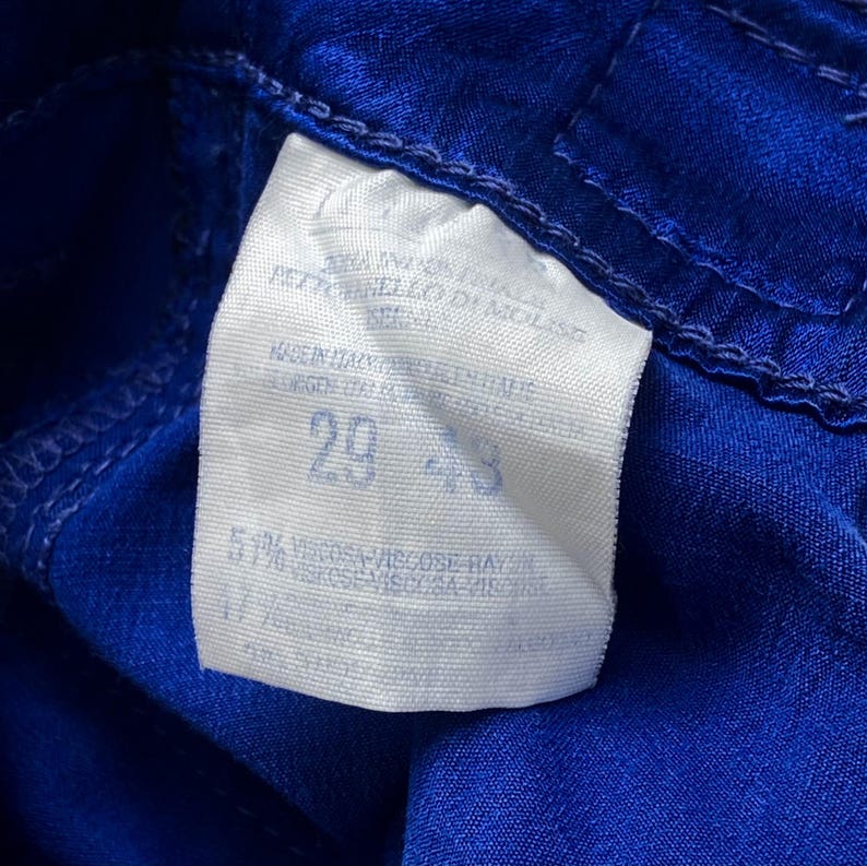 May include: Close-up of a white tag with the number 29 and 43 printed on it, sewn onto a vibrant blue fabric. The tag also includes text indicating the fabric composition and origin.