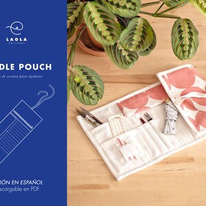 Puede incluir: Un rollo de agujas blanco y rosa con una correa blanca y un fondo blanco. El rollo está abierto y tiene varios compartimentos para agujas y otras herramientas de costura. El texto "PATRÓN EN ESPAÑOL Descargable en PDF" está impreso en la parte inferior de la imagen.