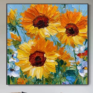 Può includere: Un dipinto a olio quadrato che raffigura tre grandi girasoli gialli vibranti con centri marrone scuro su un cielo azzurro. L'opera presenta pennellate spesse e materiche e include fiori bianchi e blu alla base del dipinto.