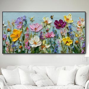 Op de afbeelding: Een rechthoekig wandkunstwerk met een dik, textuurrijk olieverfschilderij van een levendige bloemenweide. De compositie toont diverse bloemen in tinten geel, roze, paars en wit tegen een lichtblauwe achtergrond met een kleine bij.