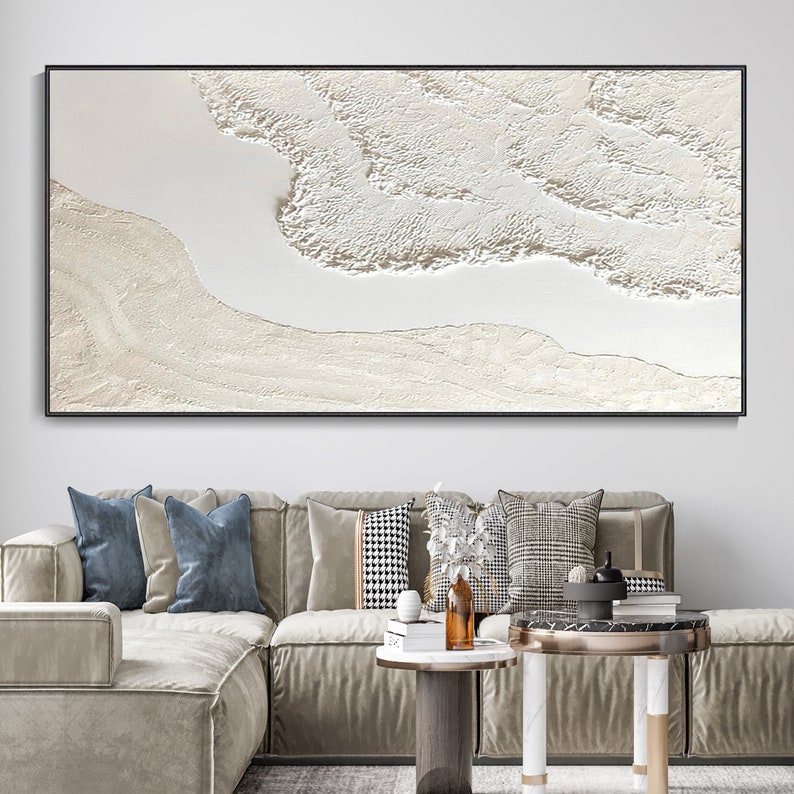 May include: A large abstract painting with a white background and a textured, raised design in shades of white and cream. The painting is framed in a black frame and is hanging on a white wall.