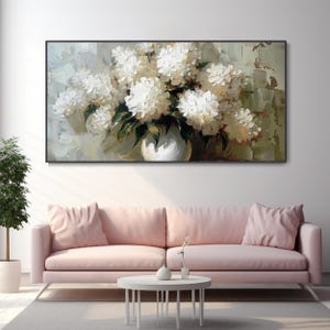 May include: A framed floral oil painting featuring a bouquet of white flowers in a white vase. The artwork has a textured, impressionistic style with green and beige background tones. The painting hangs above a pink sofa.