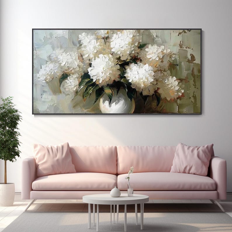 May include: A framed floral oil painting featuring a bouquet of white flowers in a white vase. The artwork has a textured, impressionistic style with green and beige background tones. The painting hangs above a pink sofa.