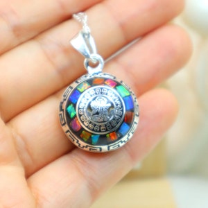 May include: A silver pendant necklace with a round, multi-colored, opal-like stone set in a silver frame. The frame is decorated with a geometric pattern and a small silver figure in the center.