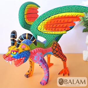 May include: A vibrant, hand-painted alebrije sculpture of a fantastical creature. The sculpture features a dragon-like body with colorful wings, horns, and intricate patterns in shades of green, orange, yellow, blue, pink, and black. The creature stands on four legs with orange feet.