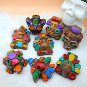 Può includere: Otto fischietti in ceramica colorati, ognuno raffigurante una diversa divinità o animale Maya. I fischietti sono dipinti con colori vivaci, tra cui rosso, blu, verde, giallo, viola e arancione. I fischietti sono disposti su una superficie bianca e soffice.