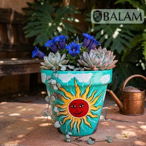 May include: A hand-painted turquoise ceramic flower pot featuring a large yellow sun with a red face and white clouds. The pot contains blue bell-shaped flowers, green succulents, and a trailing vine. The word BALAM is printed at the top.
