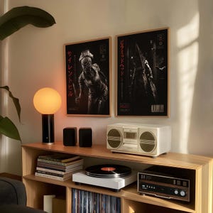 Puede incluir: Un mueble de madera con un equipo de m&uacute;sica vintage, un tocadiscos blanco y dos carteles enmarcados con texto japon&eacute;s. Una l&aacute;mpara negra y dorada y dos peque&ntilde;os altavoces negros tambi&eacute;n est&aacute;n presentes. Los carteles muestran im&aacute;genes en blanco y negro.