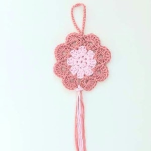 May include: A pink and light pink crocheted flower with a long tassel hanging from the bottom.