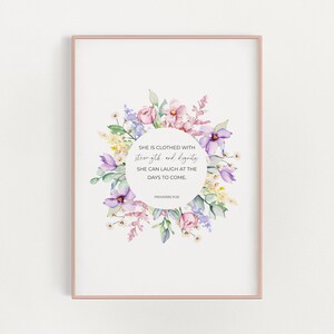 Può includere: Una ghirlanda di fiori ad acquerello con fiori viola, rosa e gialli circonda un cerchio bianco con il testo "SHE IS CLOTHED WITH strength and dignity SHE CAN LAUGH AT THE DAYS TO COME. PROVERBS 31:25"
