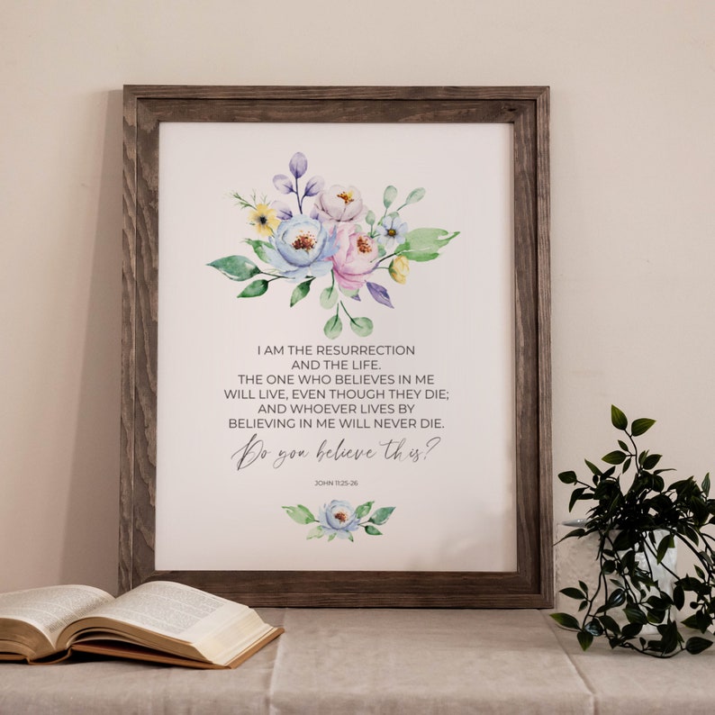 May include: Framed print with a watercolor floral design in pastel colors. The print features the text "I AM THE RESURRECTION AND THE LIFE... Do you believe this?" in a script font. The frame is a rustic, dark wood.