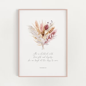Op de afbeelding: Een ingelijste print met een aquarel illustratie van een boeket gedroogde bloemen in roze, beige en bruine tinten. De print bevat de tekst "She is clothed with strength and dignity; she can laugh at the days to come." en "PROVERBS 31:25."