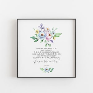 May include: Square framed print featuring a floral arrangement in pastel colors above a religious quote. The text reads "I AM THE RESURRECTION AND THE LIFE... Do you believe this?" in elegant script. The frame is black.