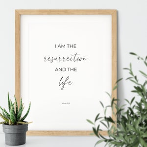May include: A framed print with a white background and black text that reads "I am the resurrection and the life" with "John 11:25" below the text.