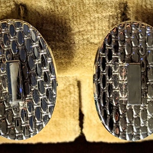 May include: A pair of silver oval cufflinks with a textured surface and a rectangular silver insert in the center.