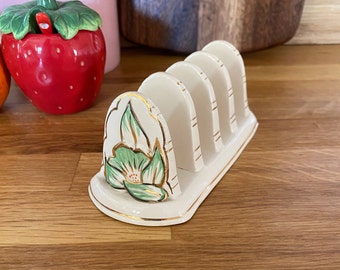 May include: A white ceramic toast rack with four slots and a green and gold floral design.