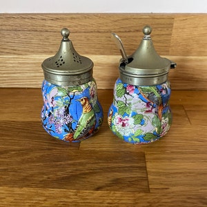 Pode incluir: Um par de saleiros e pimenteiros vintage com tampas de prata e desenhos florais azuis e brancos com pássaros. Os saleiros têm a forma de peras.