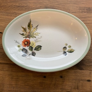 May include: A white oval serving dish with a green rim and a floral design featuring leaves, flowers, and berries.