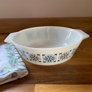 Puede incluir: Plato para hornear de cerámica blanca con un patrón geométrico azul y marrón. El plato tiene dos asas a los lados.