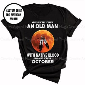 May include: Black t-shirt with the text "NEVER UNDERESTIMATE AN OLD MAN WITH NATIVE BLOOD WHO WAS BORN IN OCTOBER." The design includes a full moon and feathers. The shirt also has a custom shirt option to add a birthday month.