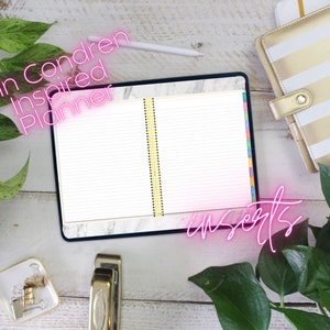 Puede incluir: Un planificador Erin Condren Inspired abierto con pestañas de colores y fondo blanco. El planificador está sobre una superficie de madera blanca con una grapadora dorada, un plato pequeño con clips dorados y dos plantas en maceta.