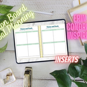 May include: A vision board and goal planning notebook with a marble cover and a green and white gridded page. The notebook is open to a page titled "Vision and Goals". The notebook is on a white wooden surface with a green plant, a gold stapler, and a gold and white striped notebook with the text "Erin Condren Inspired" in pink.