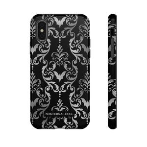 May include: Black phone case with a silver damask pattern and bats. The text "NOKTURNAL DOLL" is printed on the case.