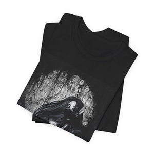 May include: Black t-shirt with a graphic print of a woman with long hair and a mask, set against a distressed, white background.