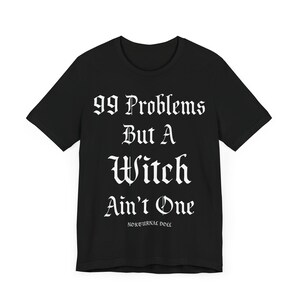 May include: Black t-shirt with white text that reads "99 Problems But A Witch Ain't One" and the words "Nocturnal Doll" in smaller font below.