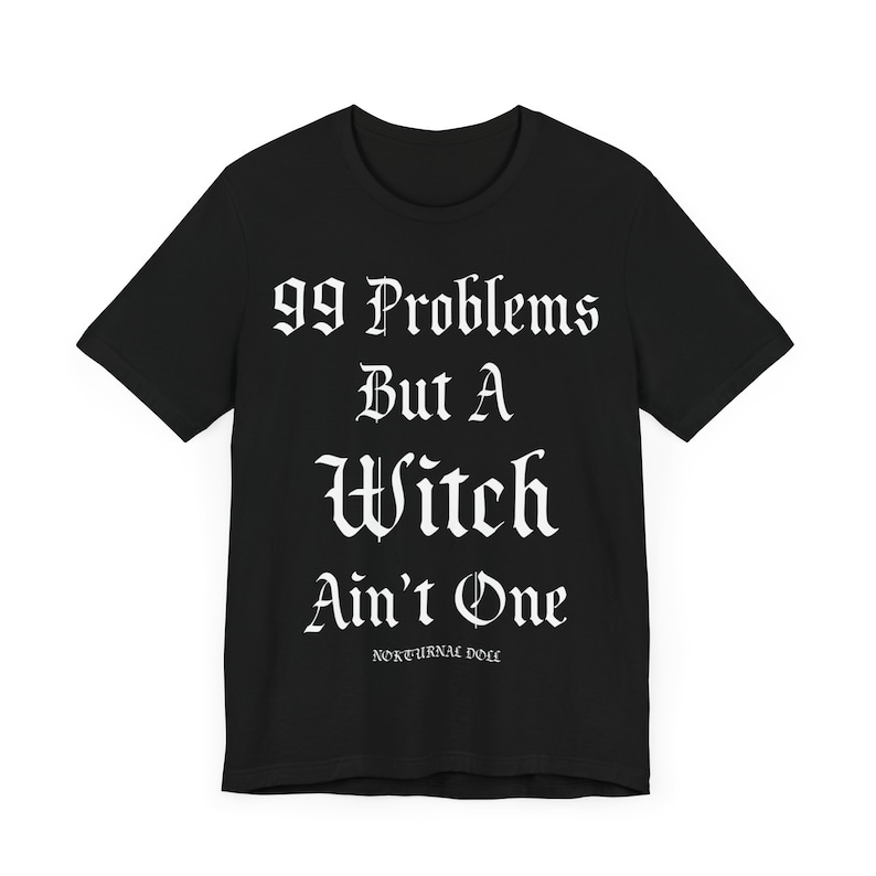 May include: Black t-shirt with white text that reads "99 Problems But A Witch Ain't One" and the words "Nocturnal Doll" in smaller font below.