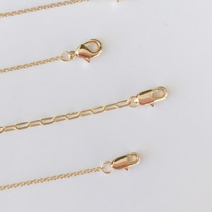 May include: Three gold chains of different lengths with lobster claw clasps. The chains are on a white surface.