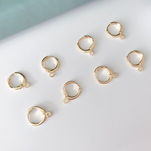 May include: Eight gold-toned earring hoops with a clasp closure. The hoops are arranged on a white surface.