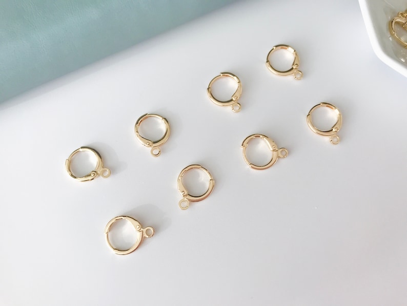 May include: Eight gold-toned earring hoops with a clasp closure. The hoops are arranged on a white surface.