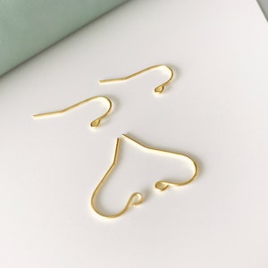 Op de afbeelding: Drie gouden oorhaken. De haken zijn van metaal en hebben een eenvoudig ontwerp.