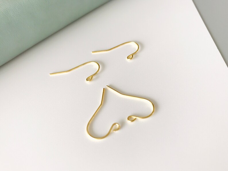 Op de afbeelding: Drie gouden oorhaken. De haken zijn van metaal en hebben een eenvoudig ontwerp.