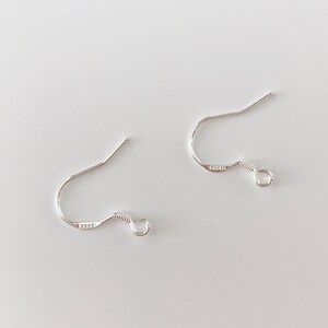 May include: Two silver earring hooks with a small loop at the end. The hooks are made of metal and are designed to be used with earrings.