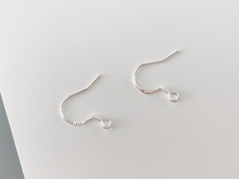 May include: Two silver earring hooks with a small loop at the end. The hooks are made of metal and are designed to be used with earrings.