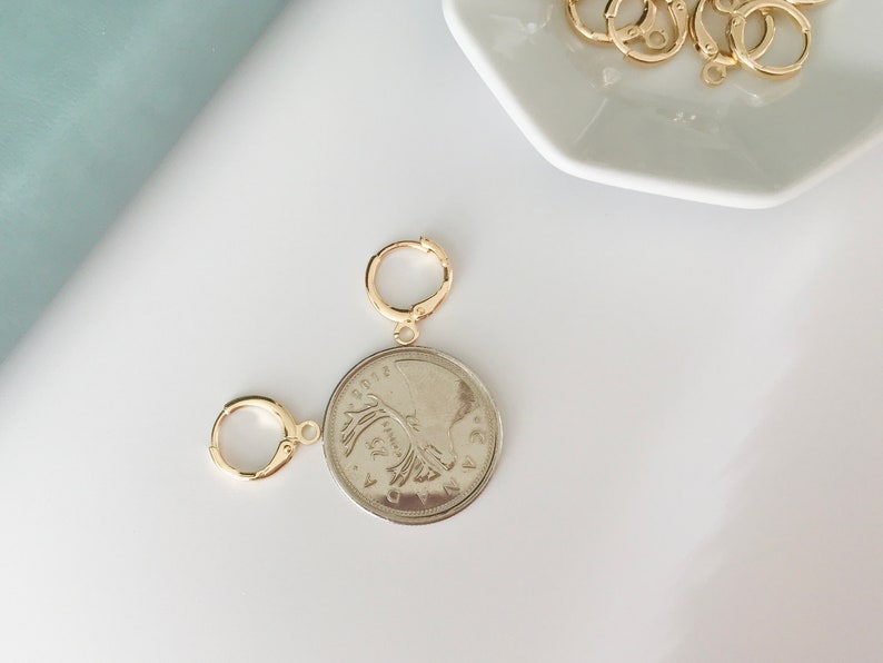 May include: A gold coin pendant with a portrait of a woman on one side and a design on the other side. The pendant is attached to a gold jump ring.